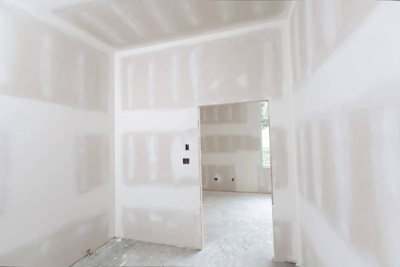 Unfinished room with drywall installed, seams and screw holes taped and mudded, open doorway leads to another room, bare concrete floor—perfect for those seeking expert Rebuild Services to complete your space.
