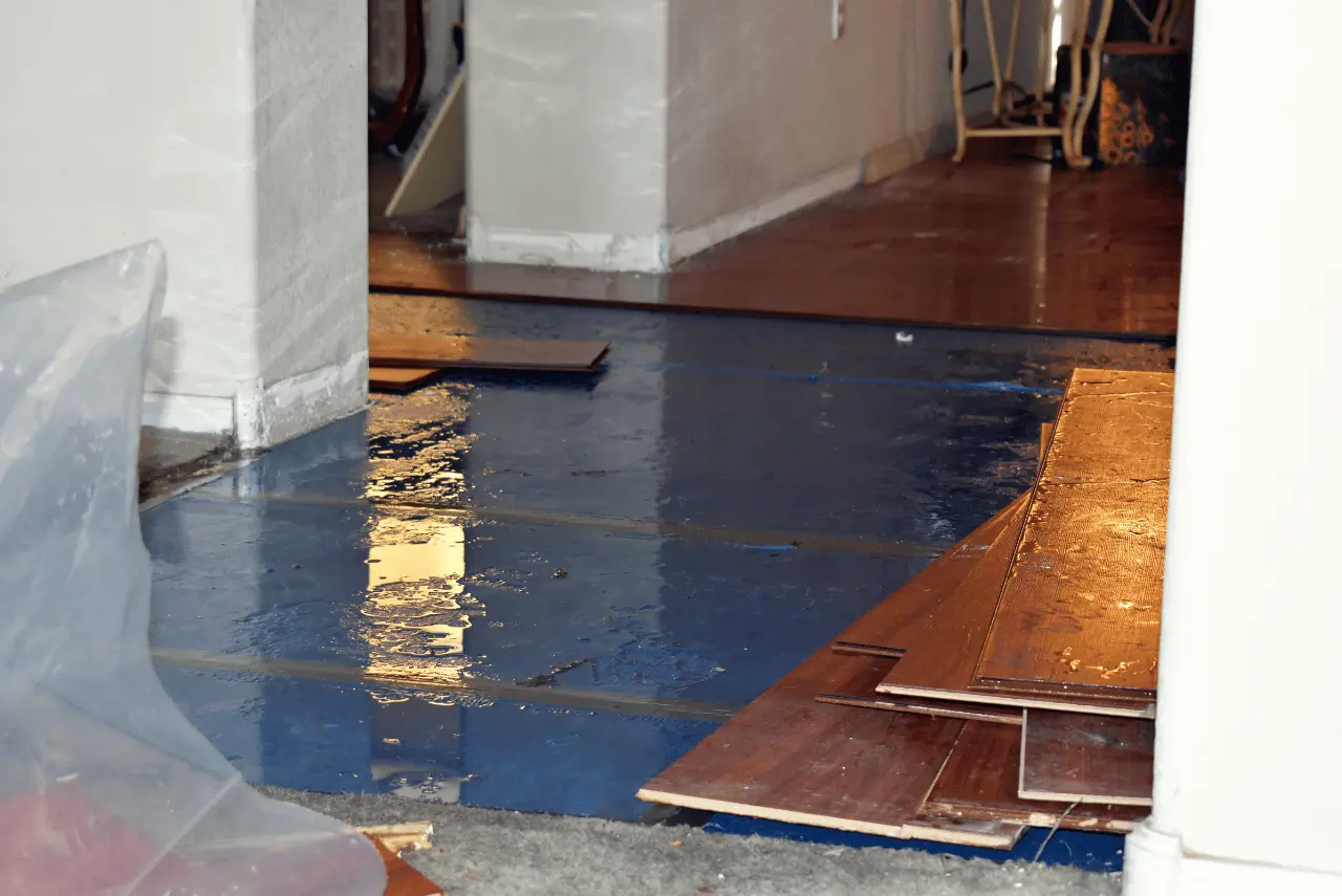 Flooded indoor floor with standing water, partially removed hardwood planks, and tools visible in the background, indicating ongoing repair work by a trusted Calgary Restoration Company.