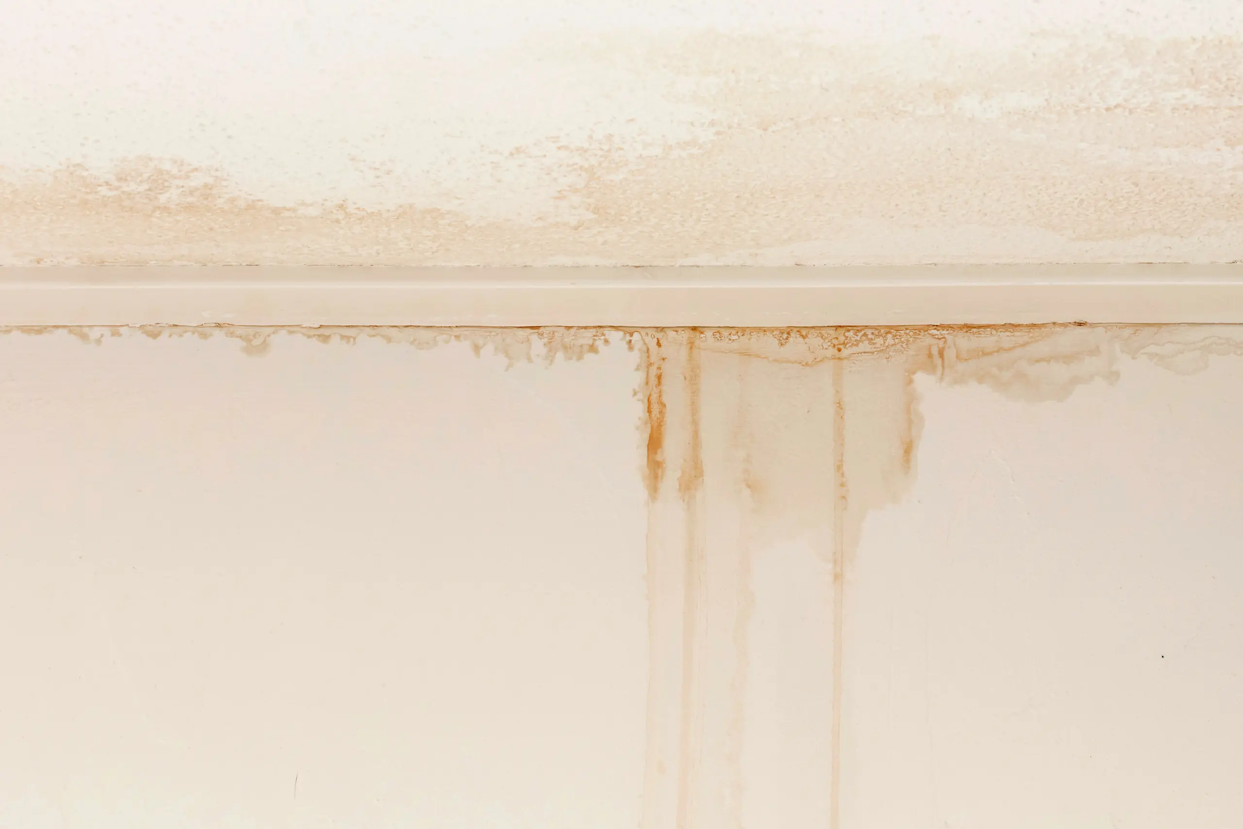 Stained white wall and ceiling with visible brown water damage and streaks, helping to recognize possible leakage or slow leaks that may be causing ongoing moisture issues.