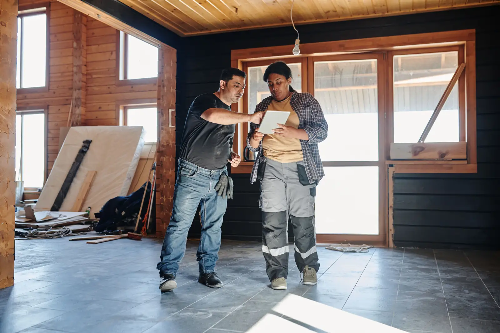 Two contractors reviewing renovation plans on a tablet indoors